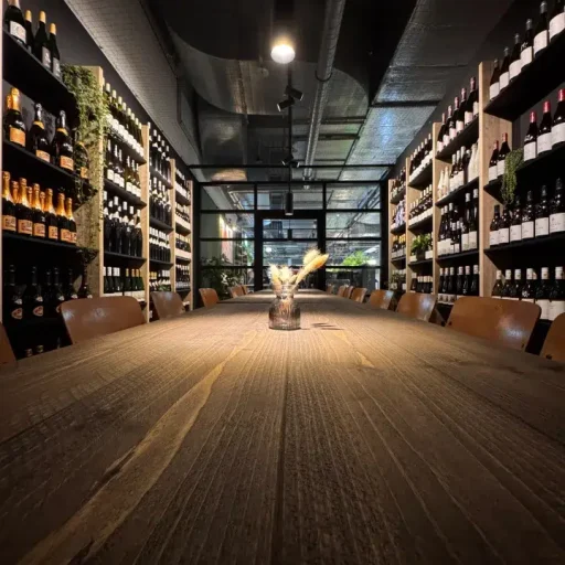 Langer gedeckter Holztisch im eleganten Weinraum der Markthalle im Königshof, umgeben von hohen Regalen voller Weinflaschen.
